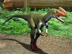 Restoration of Proceratosaurus in a forest habitat, facing the viewer at an oblique angle. Ferns and a fallen tree are visible in the background. The colouration of the animal is overall green, with a red head, hands and feet.