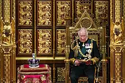 Charles seated on the Sovereign's Throne in the House of Lords during the 2022 state opening of the British Parliament. Next to him is the Imperial State Crown.