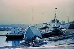A dock containing a capsized small vessels between and in front of two coast guard vessels