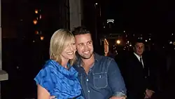 Kaitlin Olson is standing next to her husband in front of a building at night, smiling for a photograph