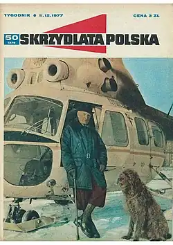 The front cover of a magazine showing a man and dog standing next to a helicopter