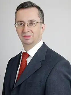 Man with short-cropped hair and wearing spectacles and a charcoal grey suit