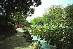 The Shizilin Garden in Suzhou. Men and women stand on curving rock formations overlooking a pond containing flowery plants.