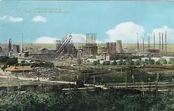 A colorised photograph of all of the multiple buildings of a steel factory