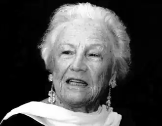 Black and white portrait of Silvana Lattmann. Head and shoulders of distinguished older woman with scarf draped elegantly over neck. She has short light-coloured hair and is wearing dangling earrings.