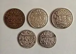 Silver Rupee coins of the Bengal Presidency, struck in the name of Mughal emperor Shah Alam II; From top left: Rupee of George Saunders' issue of 1819 (Calcutta), Broad rimmed Rupee of Farrukhabad, Narrow rimmed Rupee of Farrukhabad, Rupee of Murshidabad from the 1780s, Rupee of Muhammadabad Benaras with the inverted mace symbol and rare fish mint mark.