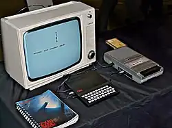 ZX81 in between a copy of the "ZX81 BASIC Programming" manual and a cassette tape recorder, with a black-and-white Ferguson TV set on the background.