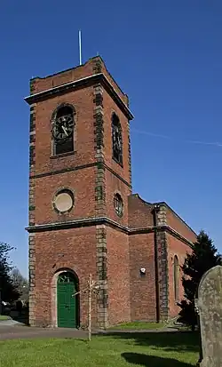 Red brick building with imposing tower having a clock and light natural quoin stone accents, many of which are pollution darkened, on a sunny day against a deep blue sky