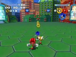 Gameplay screenshot from Sonic Heroes. In it, the cartoonish animals Sonic, Tails, and Knuckles run on top of a building in the Grand Metropolis level; there are gold rings and red hovering robots in front of them. The background depicts high-tech buildings and more of the level's geometry. The score, time, and rings collected are in the upper left corner.