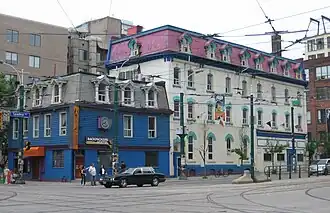 Three-storey building in the foreground painted royal blue and grey, with a four-storey building in the background painted white and pink