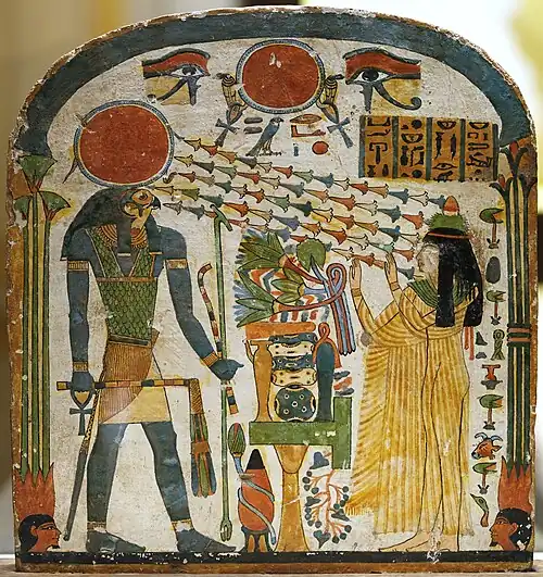 Painted wood panel showing a woman with arms upraised toward a man with a falcon's head and a sun-disk crown. Chains of flowers-like shapes radiate from the disk toward the woman's face.