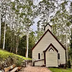 A small painted timber church among very tall eucalyptus trees.