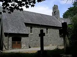 Part of a stone church with a large slate roof seen from a slight angle; on the left is a slightly protruding porch with wooden gates, and on the summit is a bellcote