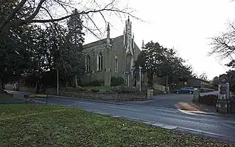 Exterior view of a stone church with a square tower, set among trees