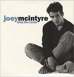 The cover features a black-and-white image of Joey McIntyre sitting down barefooted, wearing a long shirt and jeans. Both the artist's name and song title appear on the left: "Joey" and "Stay the Same" are colored in blue, "McIntyre" is colored in black.