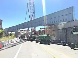 A long bridge girder being lifted into place above an expressway