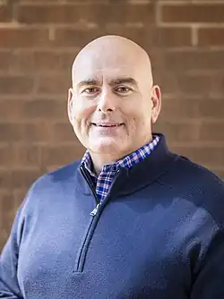 Head shot of Del Duca smiling in front of a brick wall
