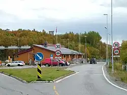 Storskog border station from the Norwegian side. Border posts are visible between the building and the dark van. A Russian watchtower can be seen on the hill in the background.