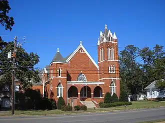 Photo of a red brick church with steeple, three arches and white painted trim.