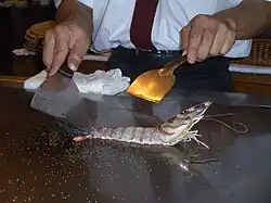 Live Jumbo Prawn on a Japanese teppan, a cook holding utensils can be seen standing behind it