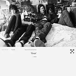 The band, in their younger years, gathers in a bed with the wall filled with cover artwork from various musicians.