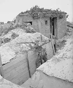 A lone soldier stands in a trench, with his rifle readied on the parapet.