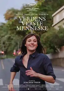 A young woman with straight brown hair and bangs, wearing a navy button-up shirt, runs joyfully down a quiet, tree-lined street with a wide smile and one hand lifted mid-stride, as text above her announces the Norwegian film "Verdens Verste Menneske" directed by Joachim Trier