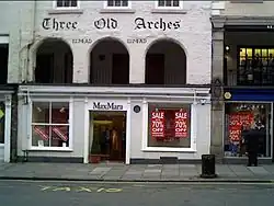 A shop front on the ground floor, above which at the first floor level are three round-headed arches. Above these is the inscription The Old Arches and the date 1274AD