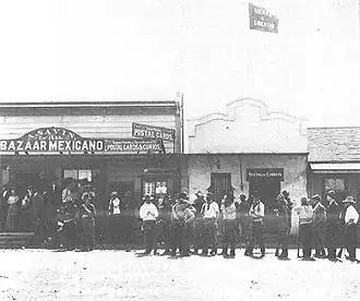 Men holding rifles, standing in front of a Mexican bazaar