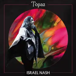 A black-and-white photo of the artist wearing a poncho, stood in front of a circle containing a psychedelic mess of colors over a plain black background.