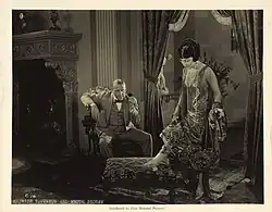 Black and white publicity photograph showing two people in formal 1920s attire