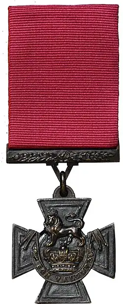 a bronze Cross pattée suspended from a crimson ribbon