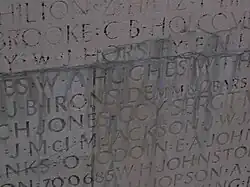 Names carved into a wall are covered in unidentified mineral deposits. Many of the names are no longer readable or are heavily distorted.