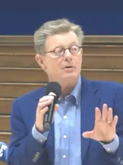 Headshot of Price gesturing with microphone in hand inside a stadium