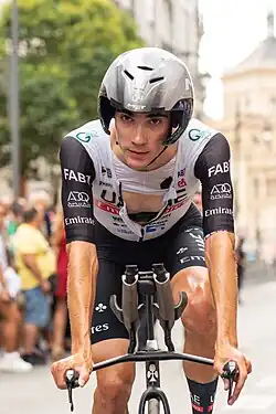 Ayuso on a time trial bike, wearing an areo-helmet and an unzipped black and white jersey.