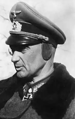 An older man wearing a peaked cap and military coat.
