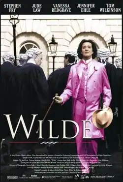 A man in a pink suit. Behind him, several judges wearing their white wigs and black cloaks, their backs turned.