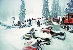 Rescuers surrounding an aircraft tail and fuselage lying in snow