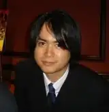 Portrait photo of a Japanese man wearing a black suit and a navy tie.