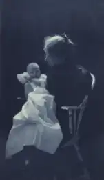 Woman sitting in chair holding an infant (1900)